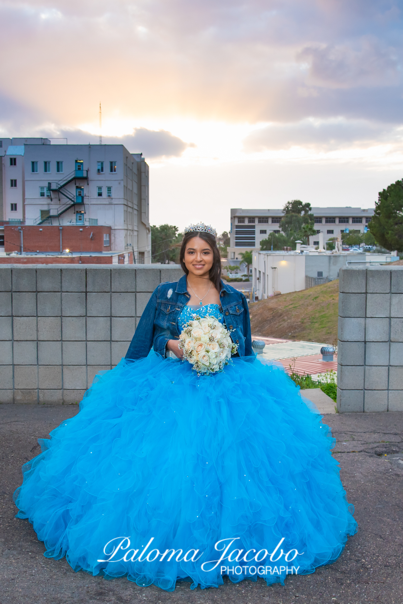 Quinceanera wearing denim jacket on urban city background at sunset by Paloma Jacobo Photography