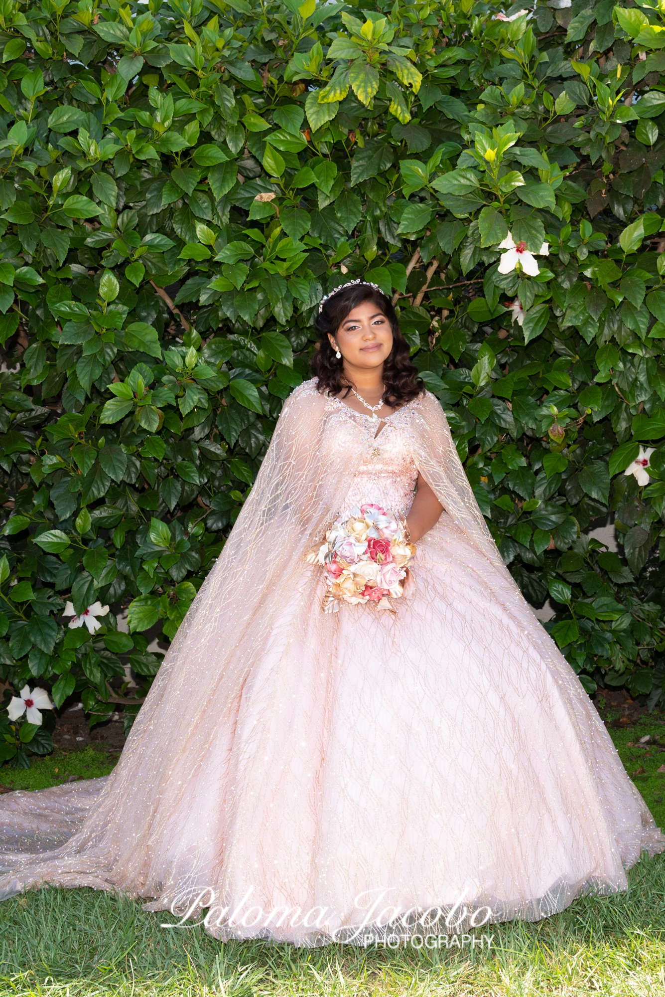 Quinceanera with a green wall background wearing a blush pink dress by Paloma Jacobo Photography