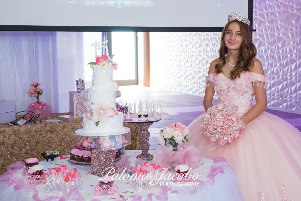 Quinceañera posando junto a su pastel blanco con el numero 15 