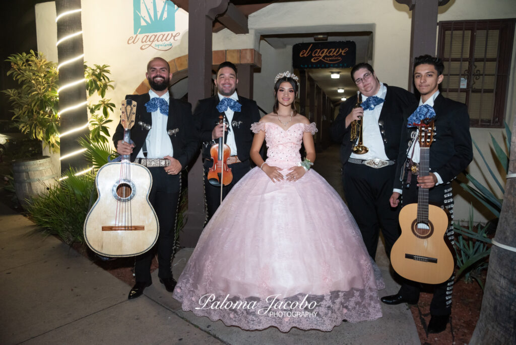 Quinceanera posing with Mariachi outside of a restaurant