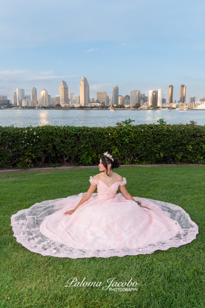 Quinceanera sitting down on the grass with the city of San Diego on the background