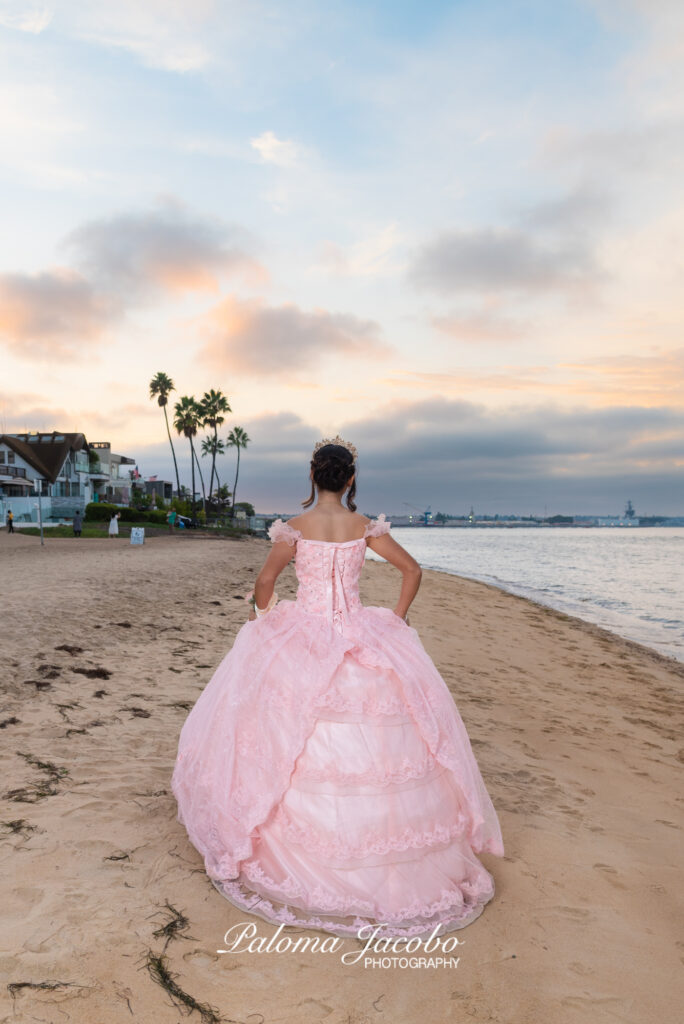 Quinceanera picture at the beach during sunset with an elegant pink dress as she walks away