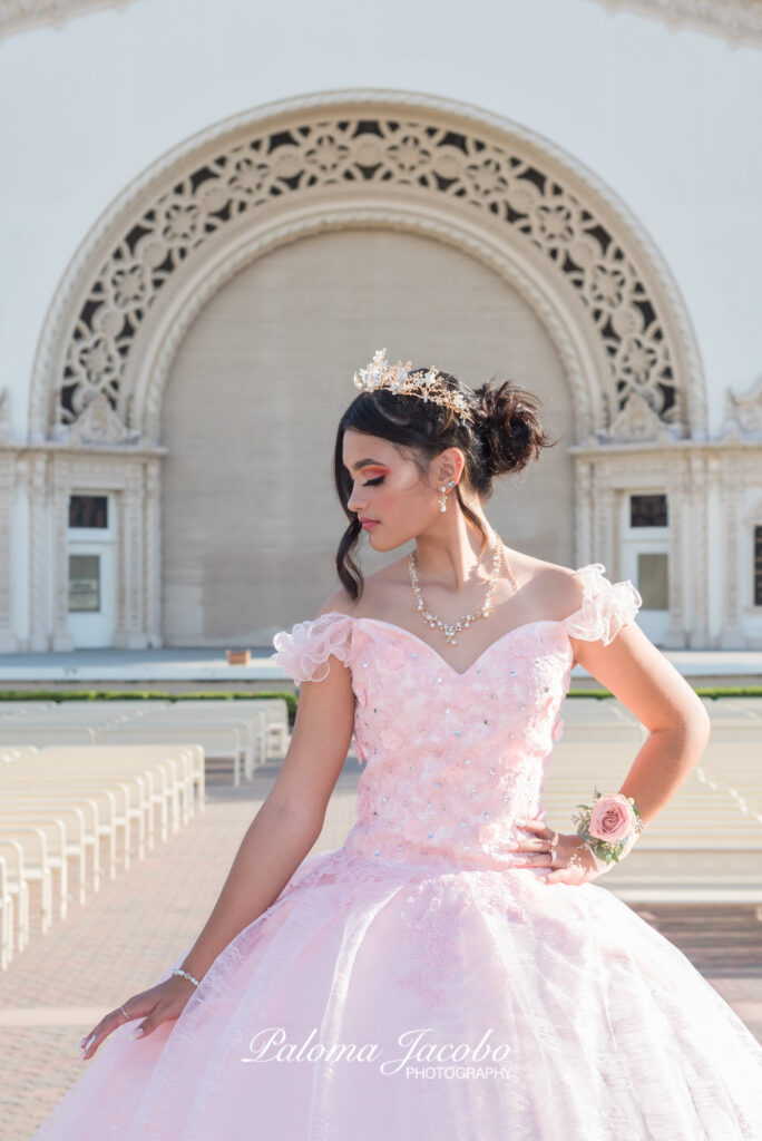 Quinceanera posing with the organ pavilion on the background wearing an elegant pink dress