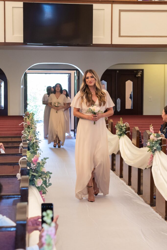 Dama de honor de 15 años entrando a la ceremonia sosteniendo un ramo de flores naturales